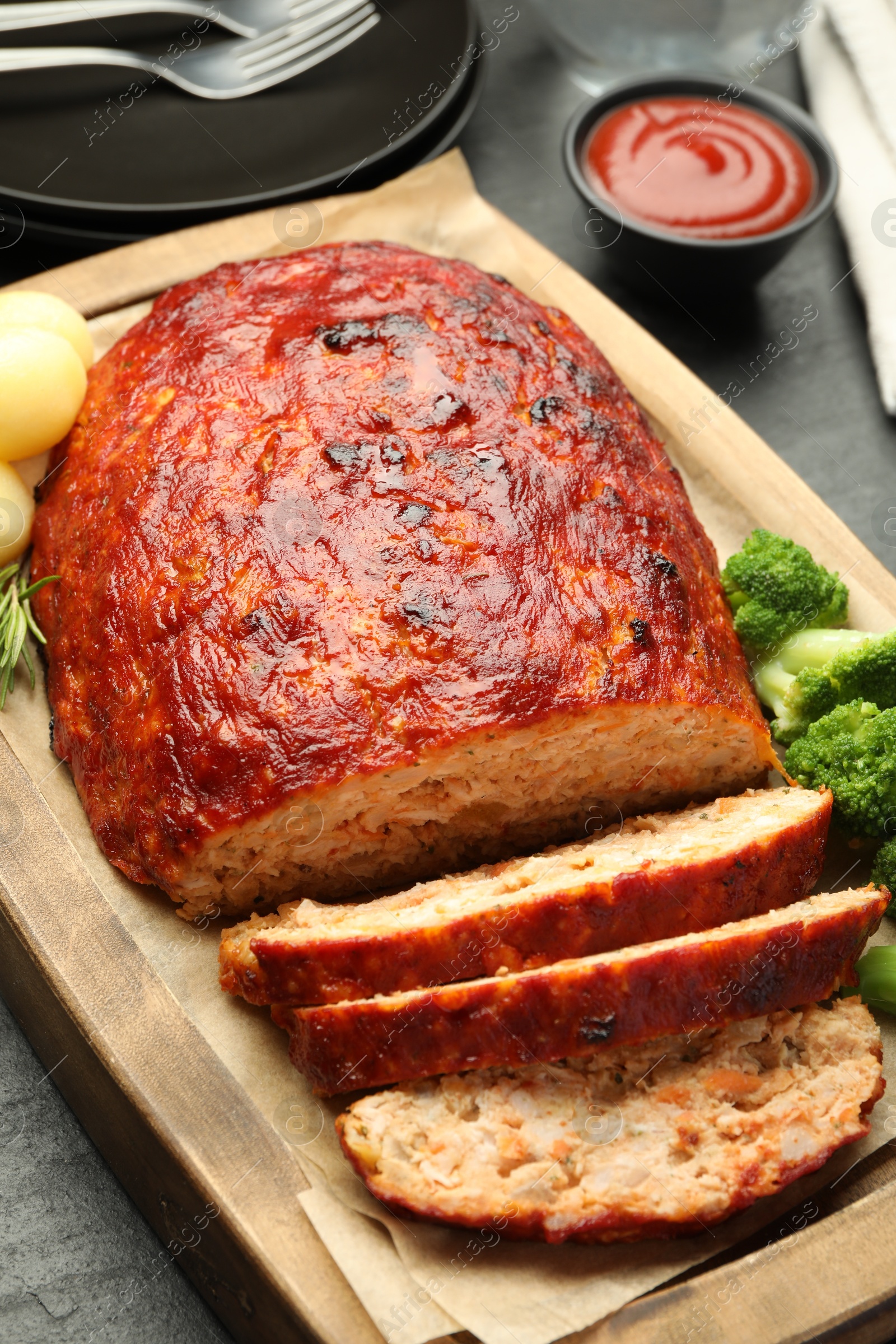 Photo of Delicious turkey meatloaf with vegetables served on black table, closeup