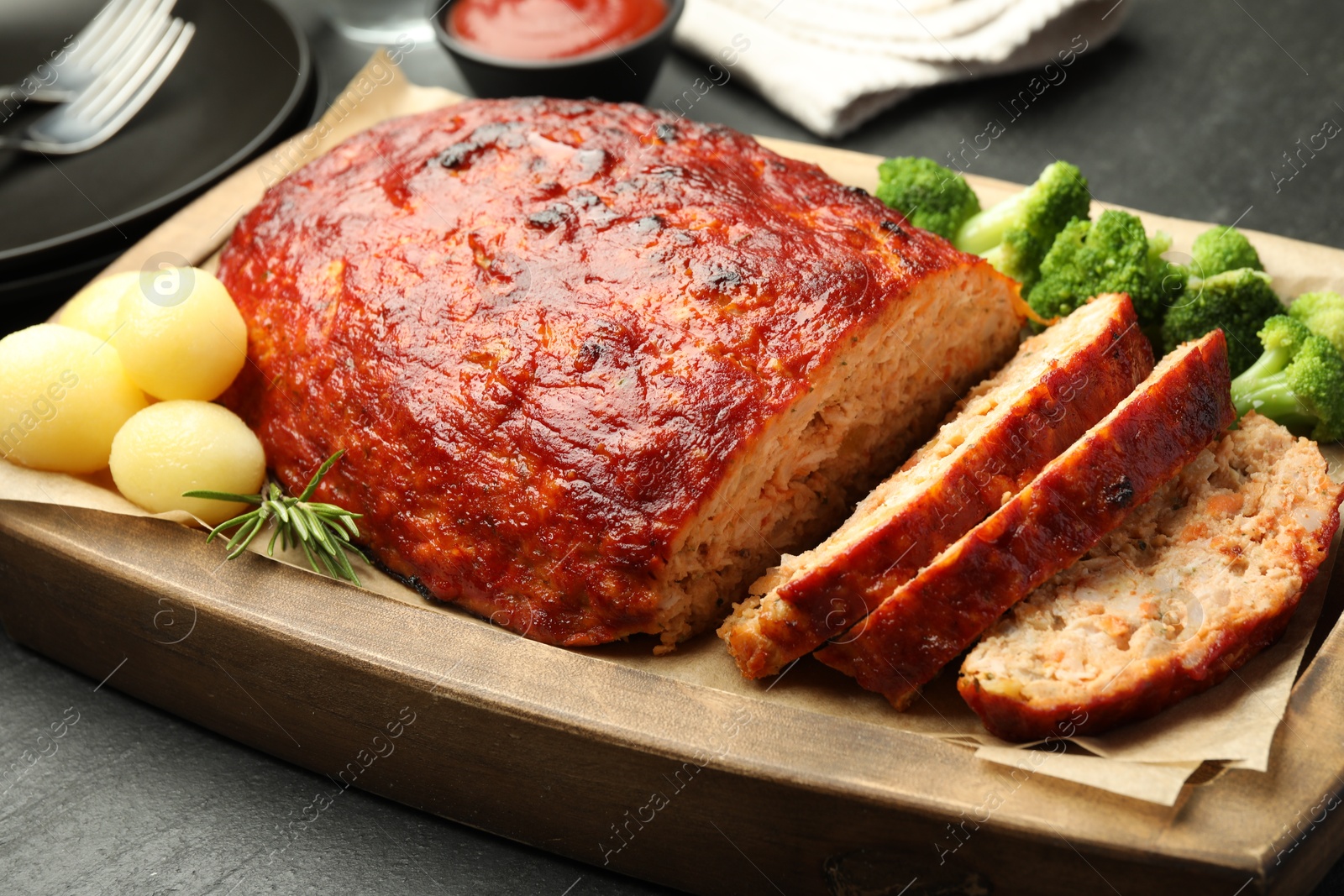 Photo of Delicious turkey meatloaf with vegetables served on black table, closeup