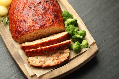 Photo of Delicious turkey meatloaf with vegetables on black table, closeup