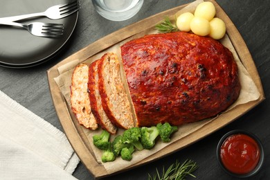 Photo of Delicious turkey meatloaf with vegetables served on black table, flat lay