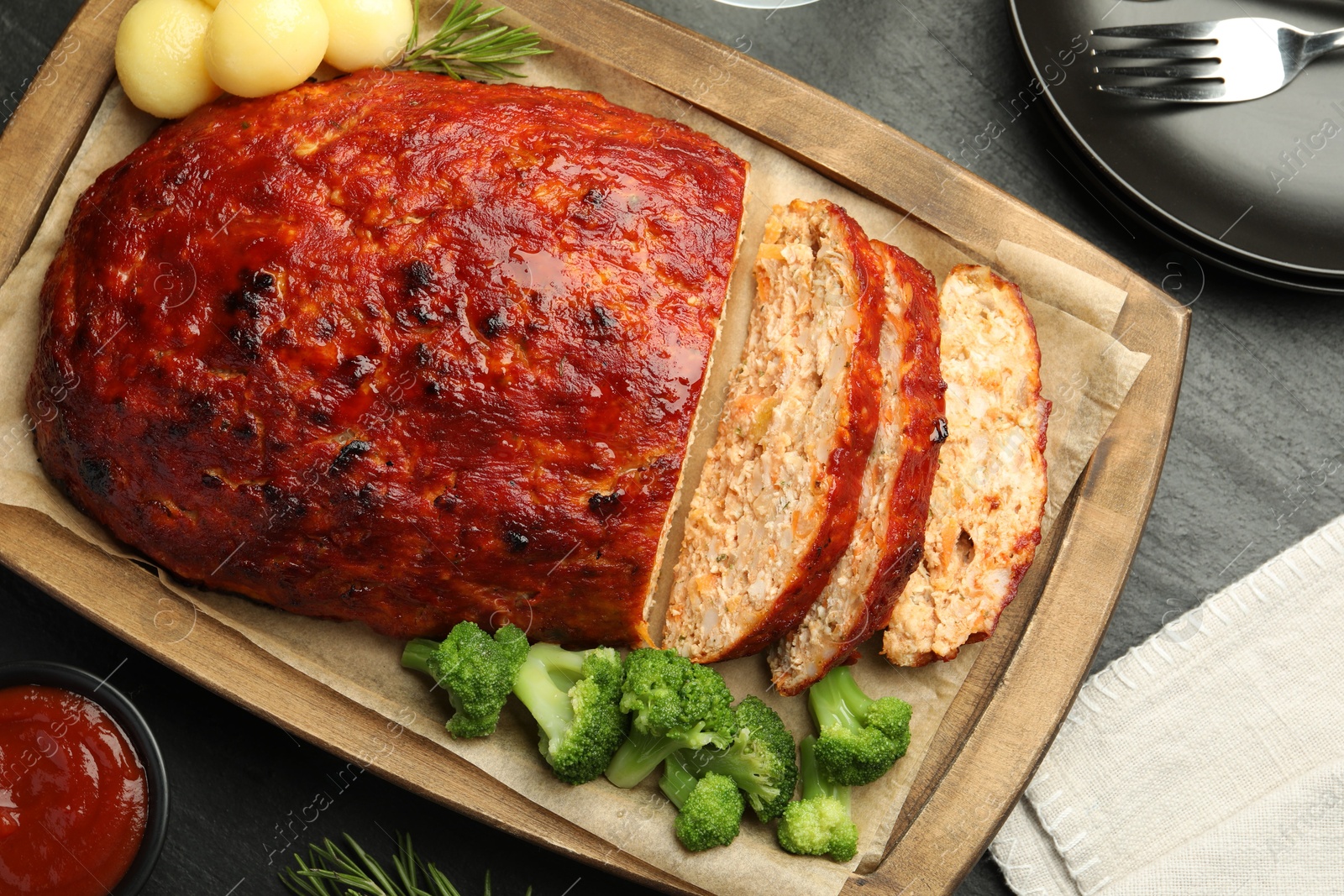 Photo of Delicious turkey meatloaf with vegetables served on black table, flat lay