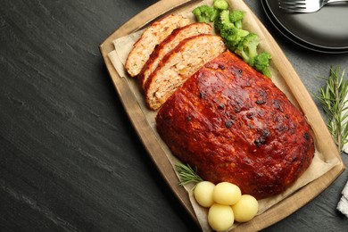 Delicious turkey meatloaf with vegetables served on black table, flat lay. Space for text