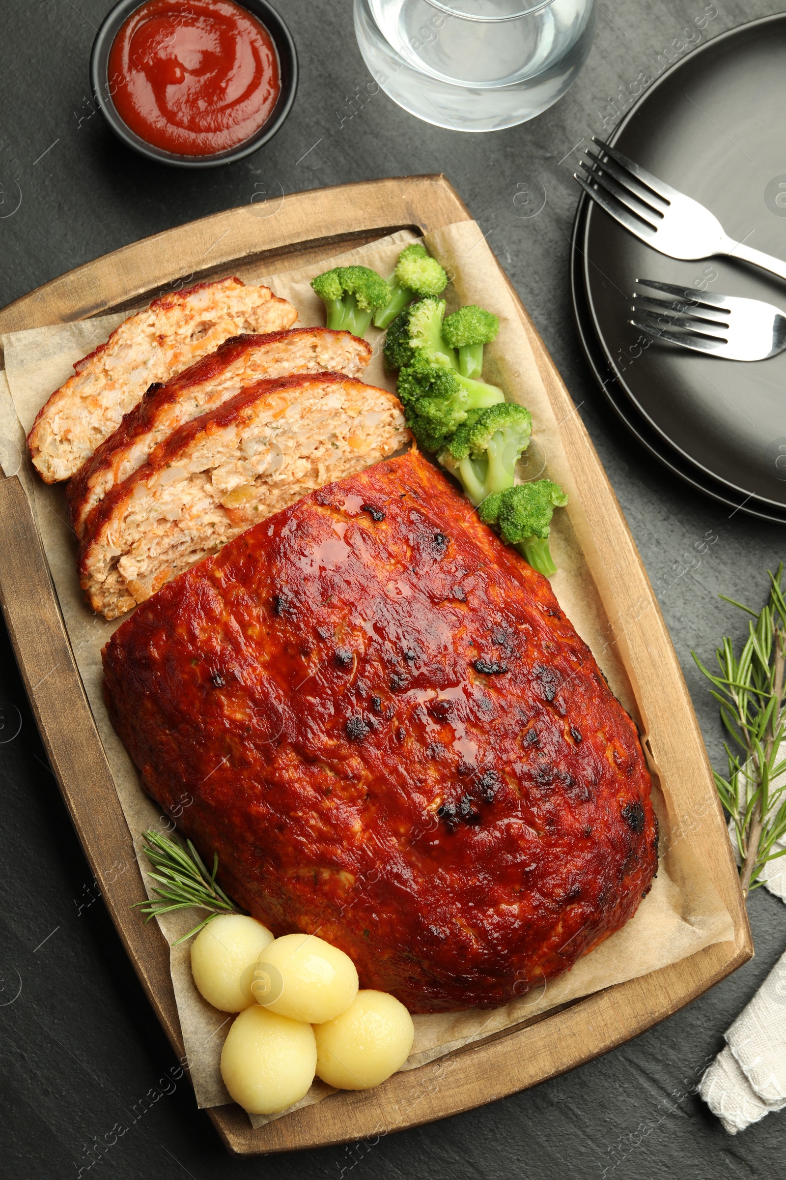 Photo of Delicious turkey meatloaf with vegetables served on black table, flat lay