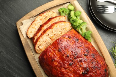 Photo of Delicious turkey meatloaf with vegetables served on black table, flat lay