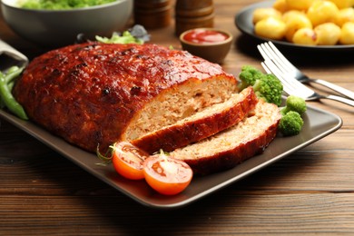 Photo of Delicious turkey meatloaf with vegetables served on wooden table, closeup