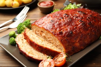 Delicious turkey meatloaf with vegetables served on wooden table, closeup