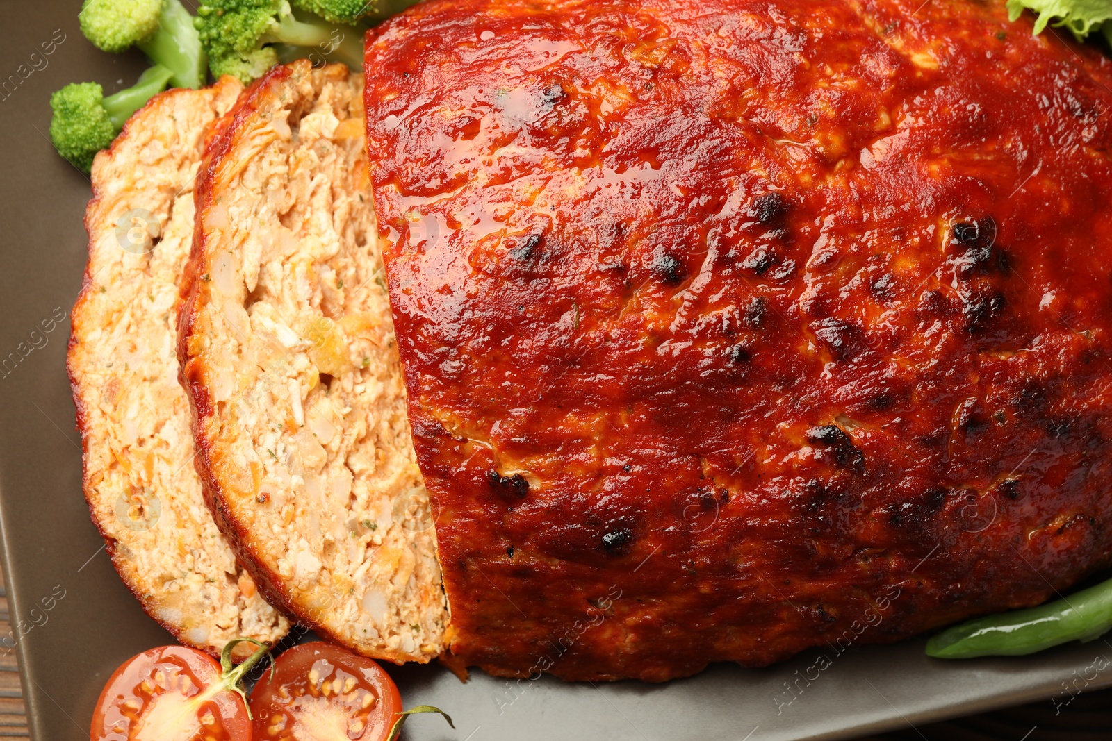 Photo of Delicious turkey meatloaf with vegetables on wooden table, closeup