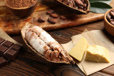 Photo of Cocoa pods with beans, chocolate and butter on wooden table, closeup