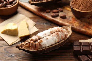 Photo of Cocoa pod with beans, chocolate and butter on wooden table, closeup