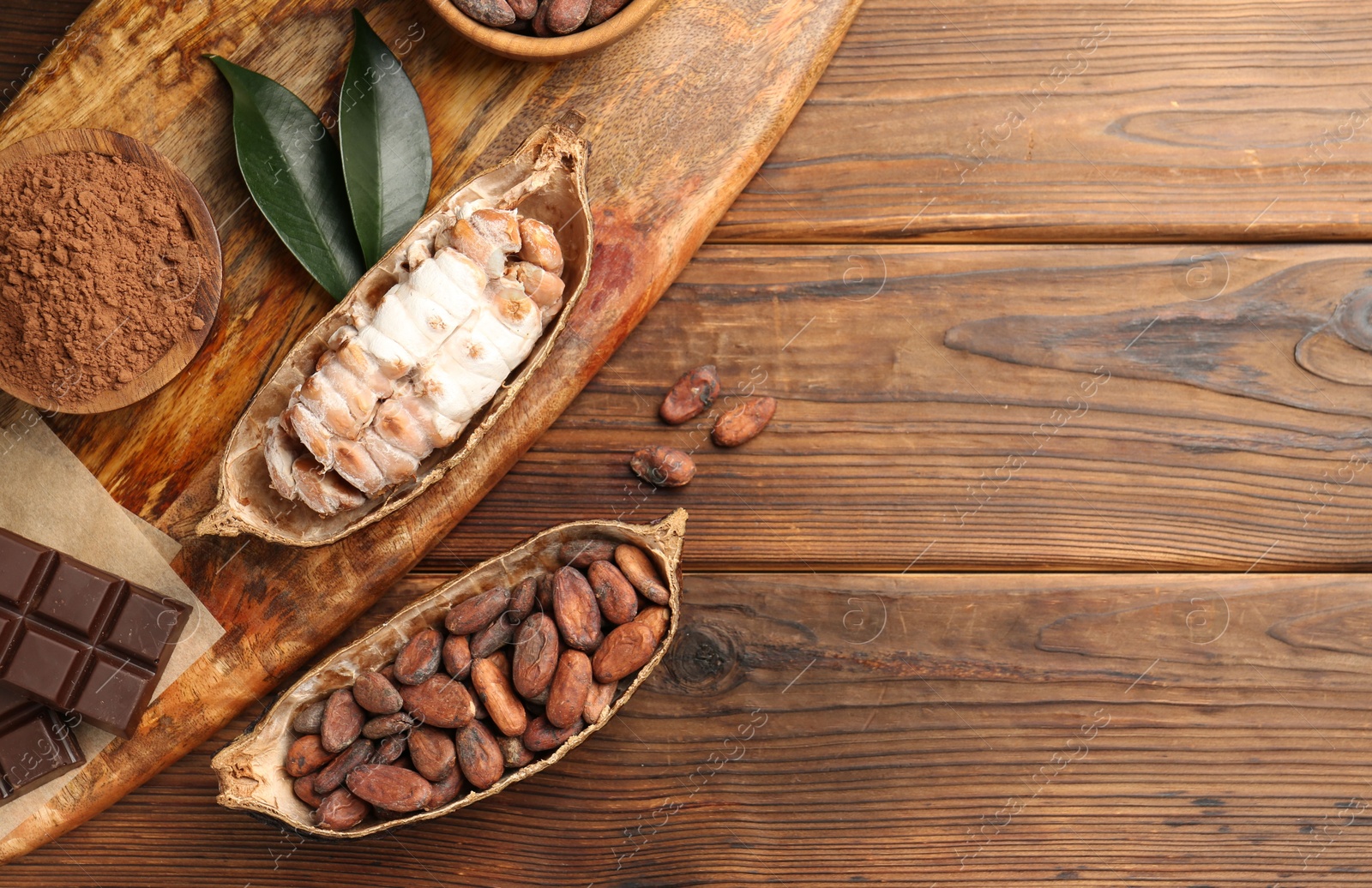 Photo of Cocoa pods with beans and chocolate on wooden table, flat lay. Space for text