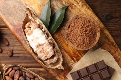 Cocoa pods with beans and chocolate on wooden table, flat lay