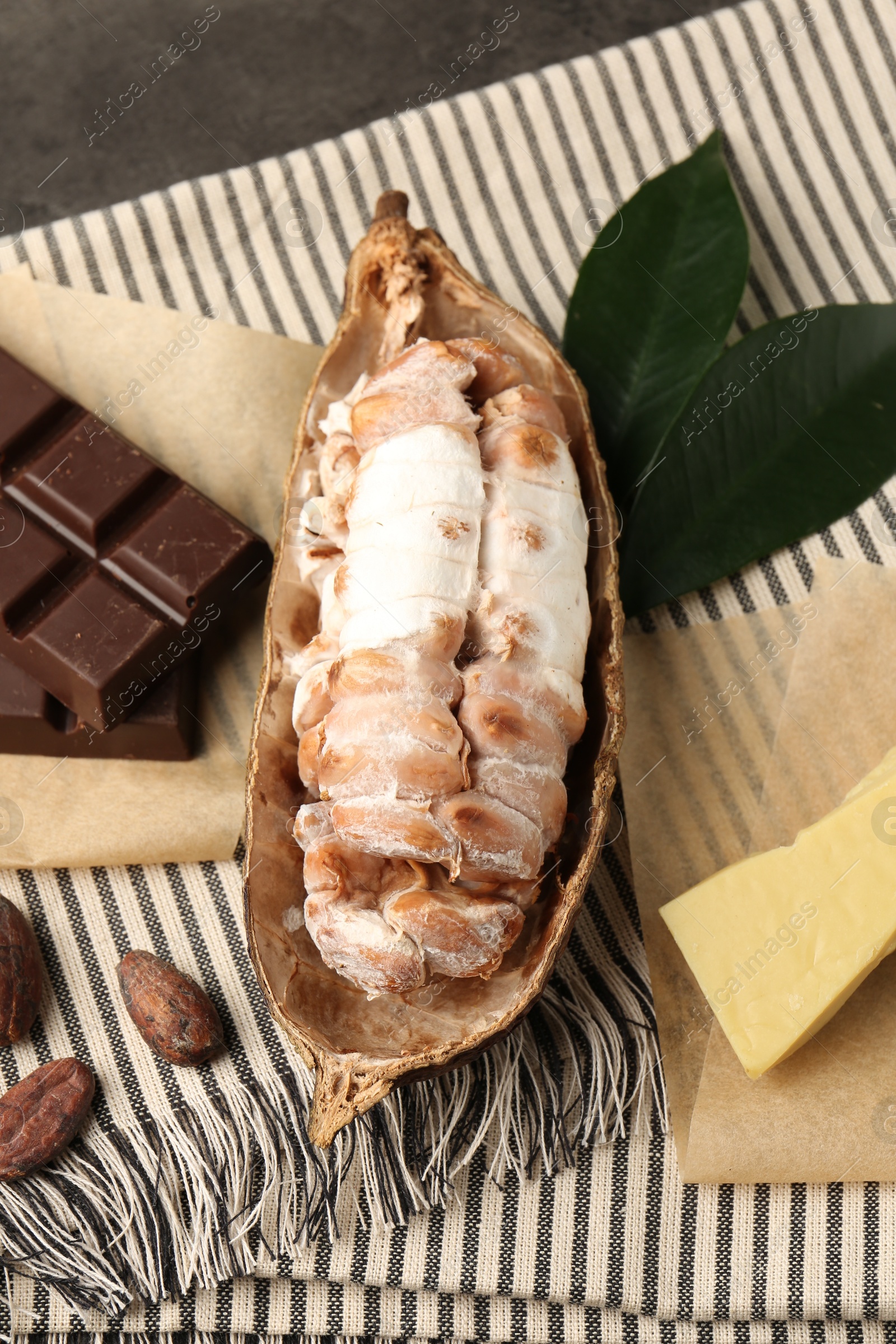 Photo of Cocoa pod with beans, butter and chocolate on grey table, closeup