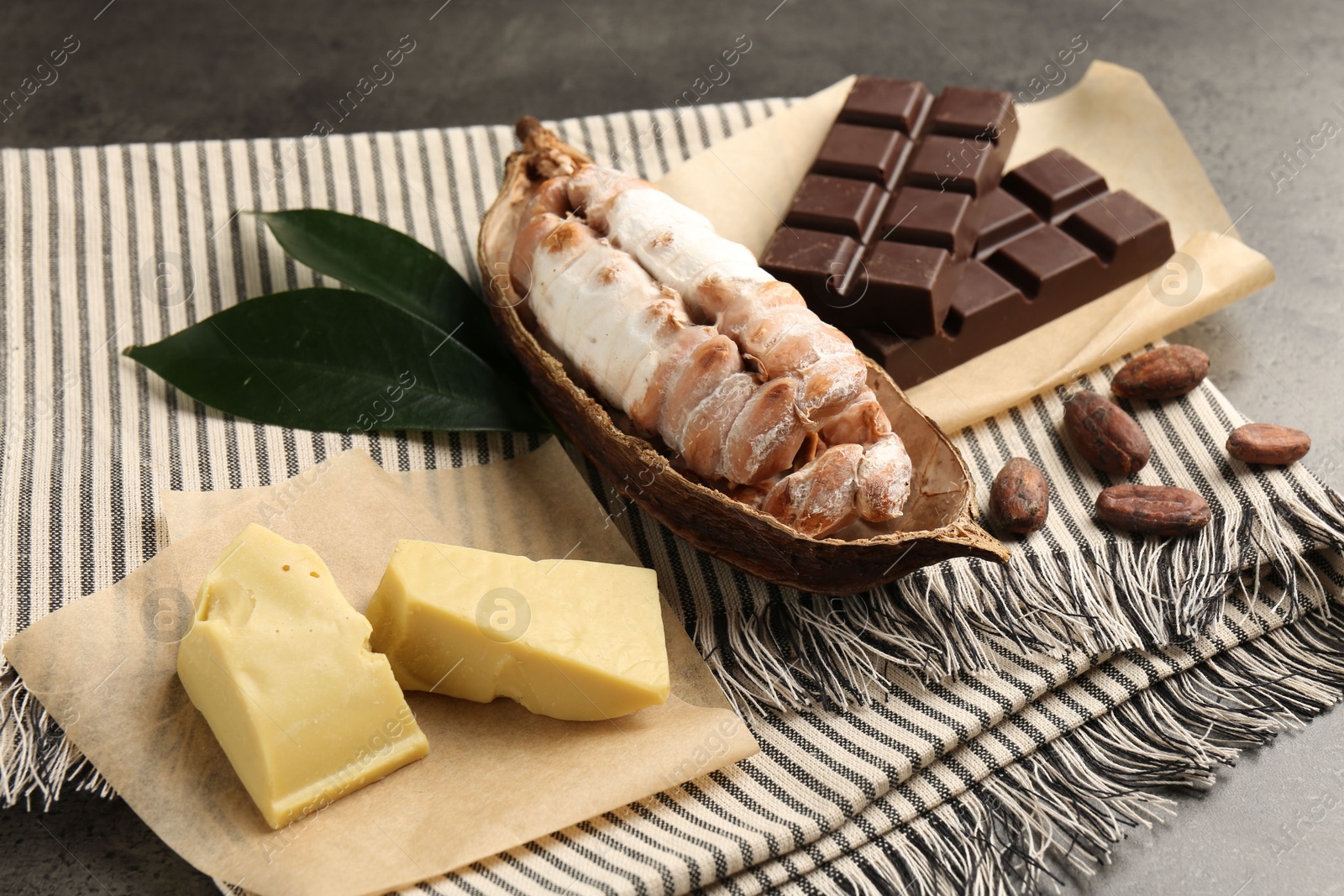 Photo of Cocoa pod with beans, butter and chocolate on grey table