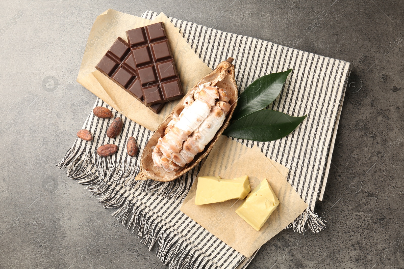 Photo of Cocoa pod with beans, butter and chocolate on grey table, flat lay