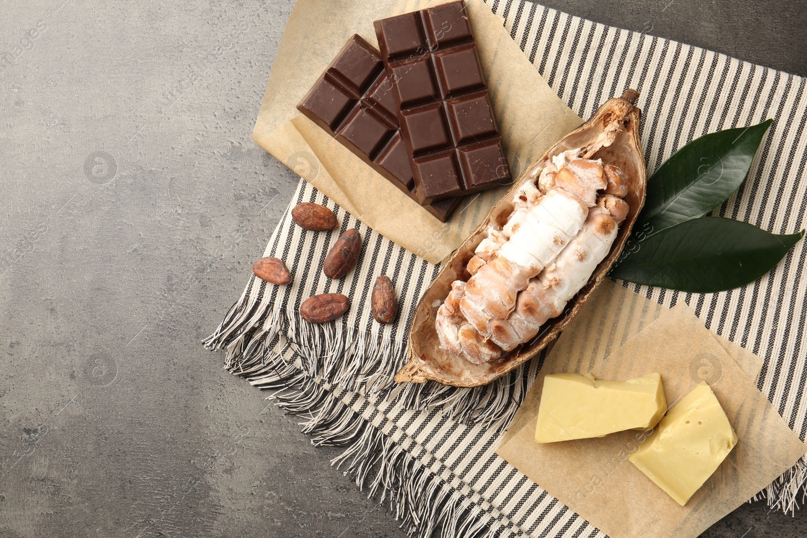 Photo of Cocoa pod with beans, butter and chocolate on grey table, flat lay. Space for text