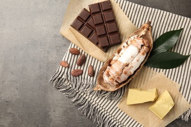 Cocoa pod with beans, butter and chocolate on grey table, flat lay. Space for text