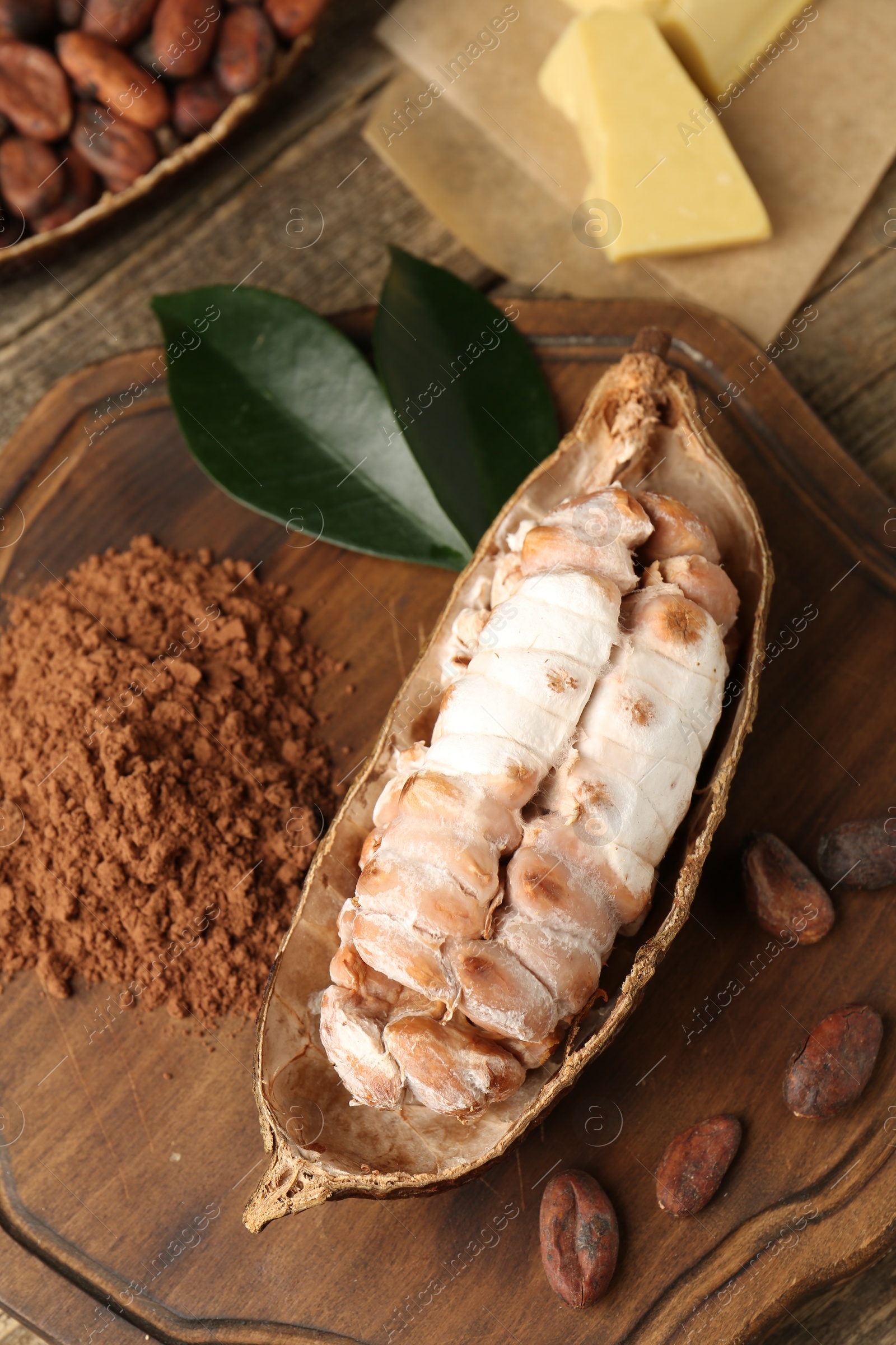 Photo of Cocoa pod with beans, powder and butter on wooden table, closeup