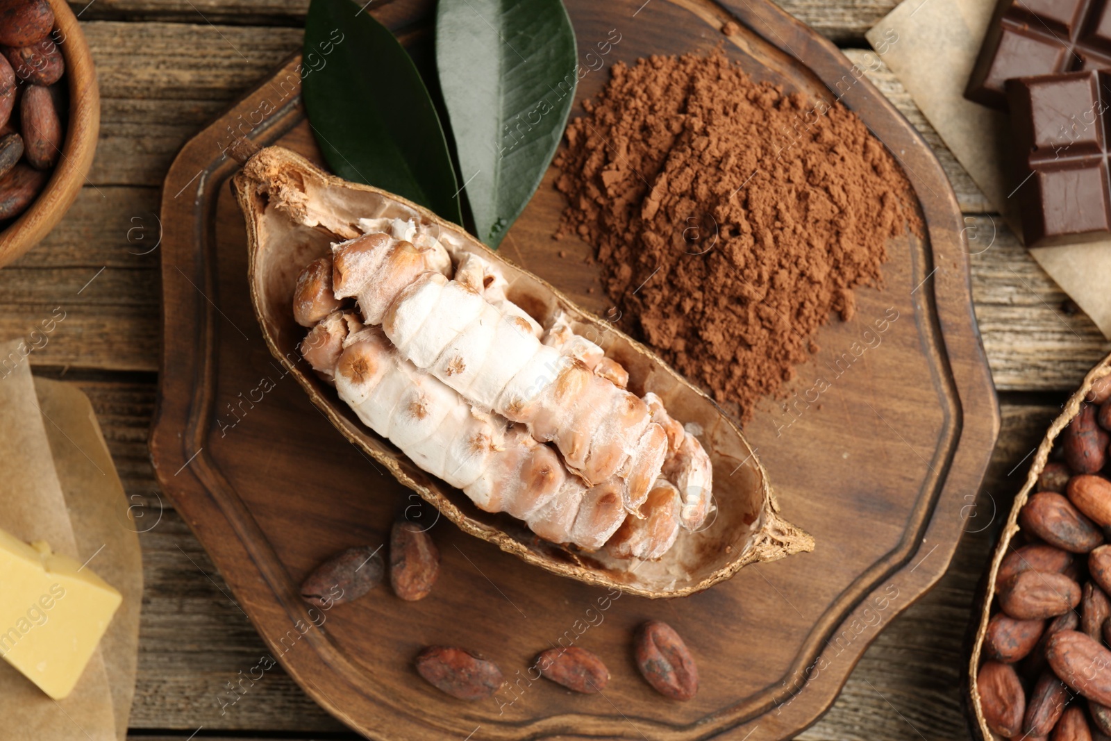 Photo of Cocoa pods with beans, powder, chocolate and butter on wooden table, flat lay