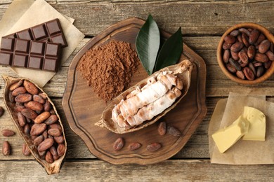 Cocoa pods with beans, powder, chocolate and butter on wooden table, flat lay