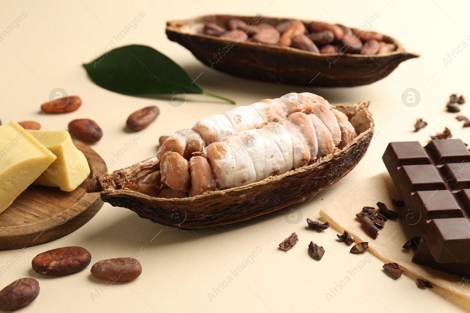 Photo of Cocoa pods with beans, butter and chocolate on beige background, closeup