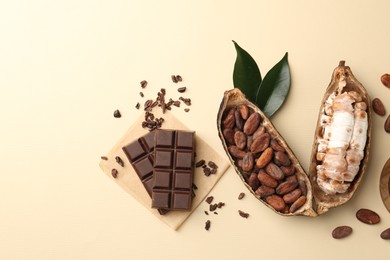 Cocoa pods with beans and chocolate on beige background, flat lay. Space for text