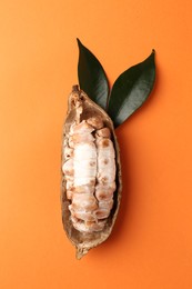 Cocoa pod with beans on orange background, top view