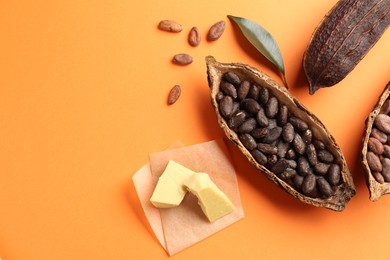 Cocoa pods with beans and butter on orange background, flat lay. Space for text