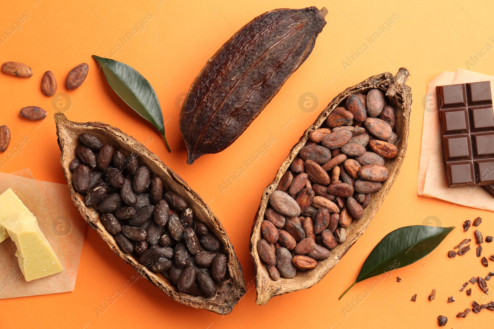 Photo of Cocoa pods with beans, chocolate and butter on orange background, flat lay