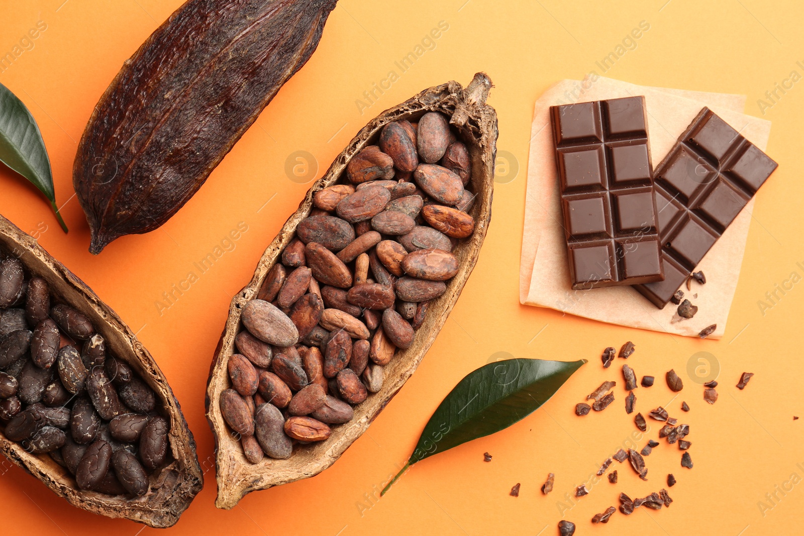 Photo of Cocoa pods with beans and chocolate on orange background, flat lay