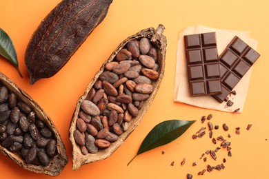 Cocoa pods with beans and chocolate on orange background, flat lay