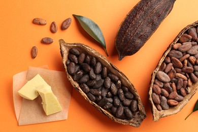 Cocoa pods with beans and butter on orange background, flat lay