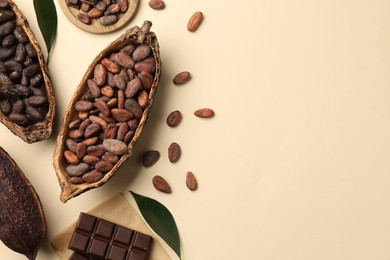 Photo of Cocoa pods with beans and chocolate on beige background, flat lay. Space for text