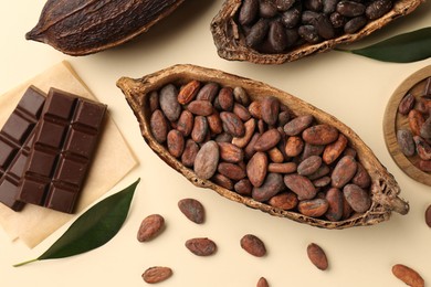 Cocoa pods with beans and chocolate on beige background, flat lay