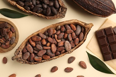 Cocoa pods with beans and chocolate on beige background, flat lay