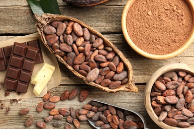 Photo of Cocoa pod with beans, powder, butter and chocolate on wooden table, flat lay