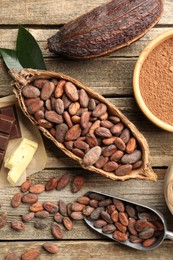 Photo of Cocoa pods with beans, powder, butter and chocolate on wooden table, flat lay