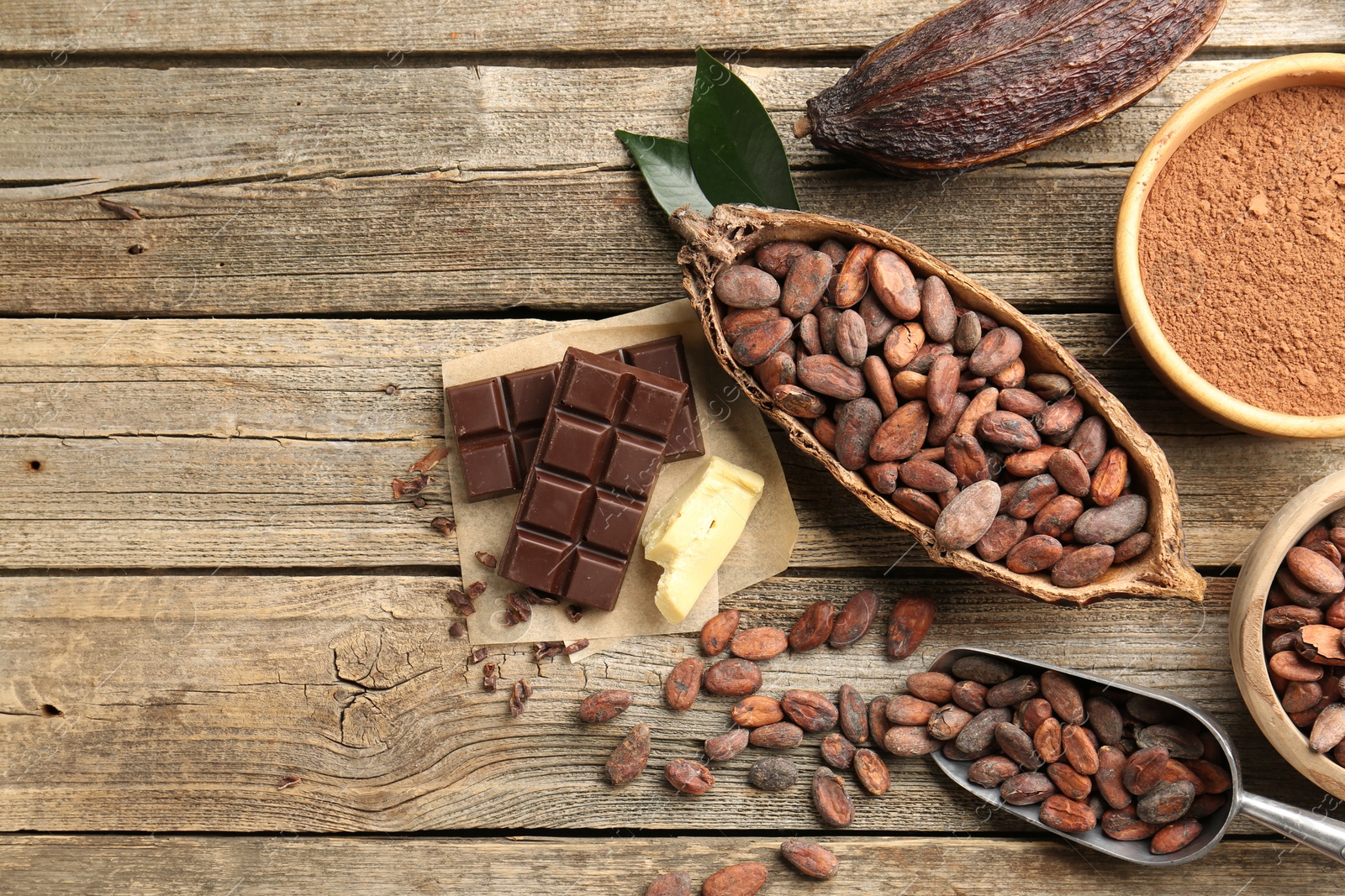 Photo of Cocoa pods with beans, powder, butter and chocolate on wooden table, flat lay. Space for text