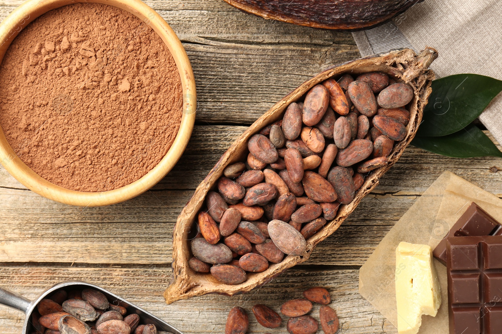 Photo of Cocoa pod with beans, powder, butter and chocolate on wooden table, flat lay