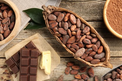 Photo of Cocoa pod with beans, powder, butter and chocolate on wooden table, flat lay