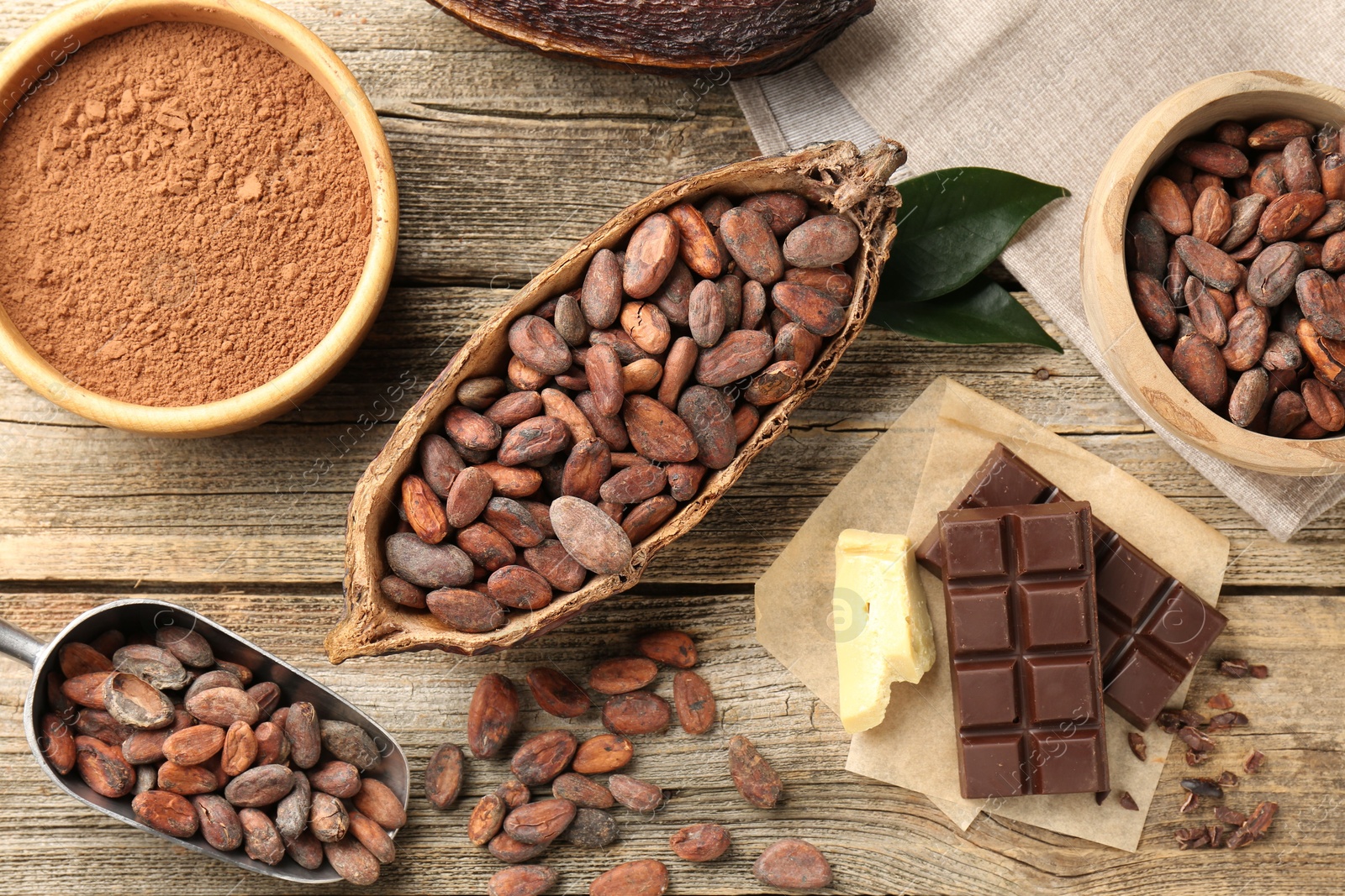 Photo of Cocoa pod with beans, powder, butter and chocolate on wooden table, flat lay