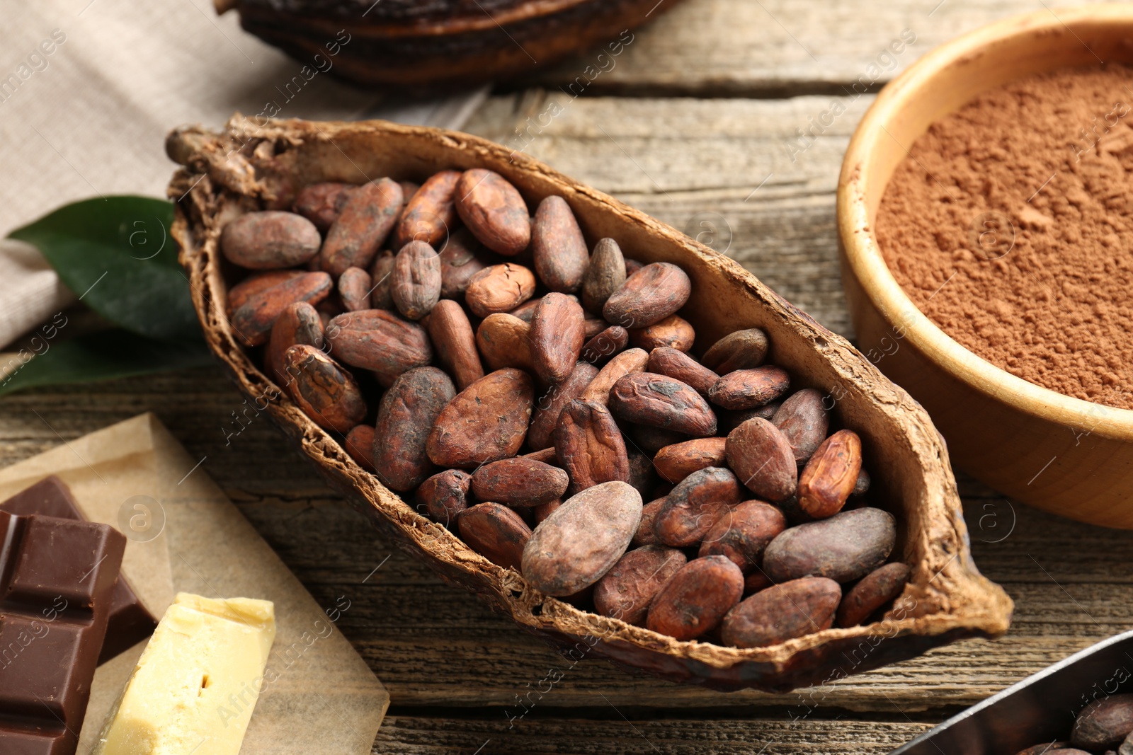 Photo of Cocoa pod with beans, powder, butter and chocolate on wooden table