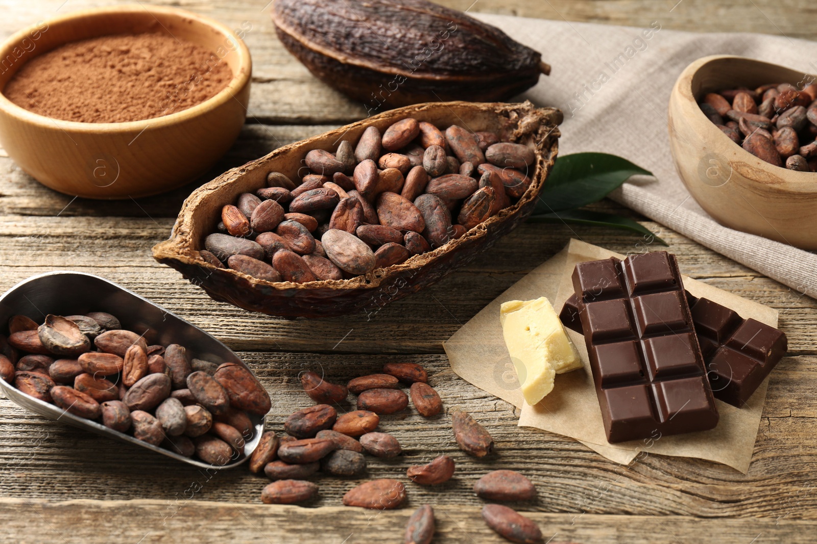 Photo of Cocoa pods with beans, powder, butter and chocolate on wooden table