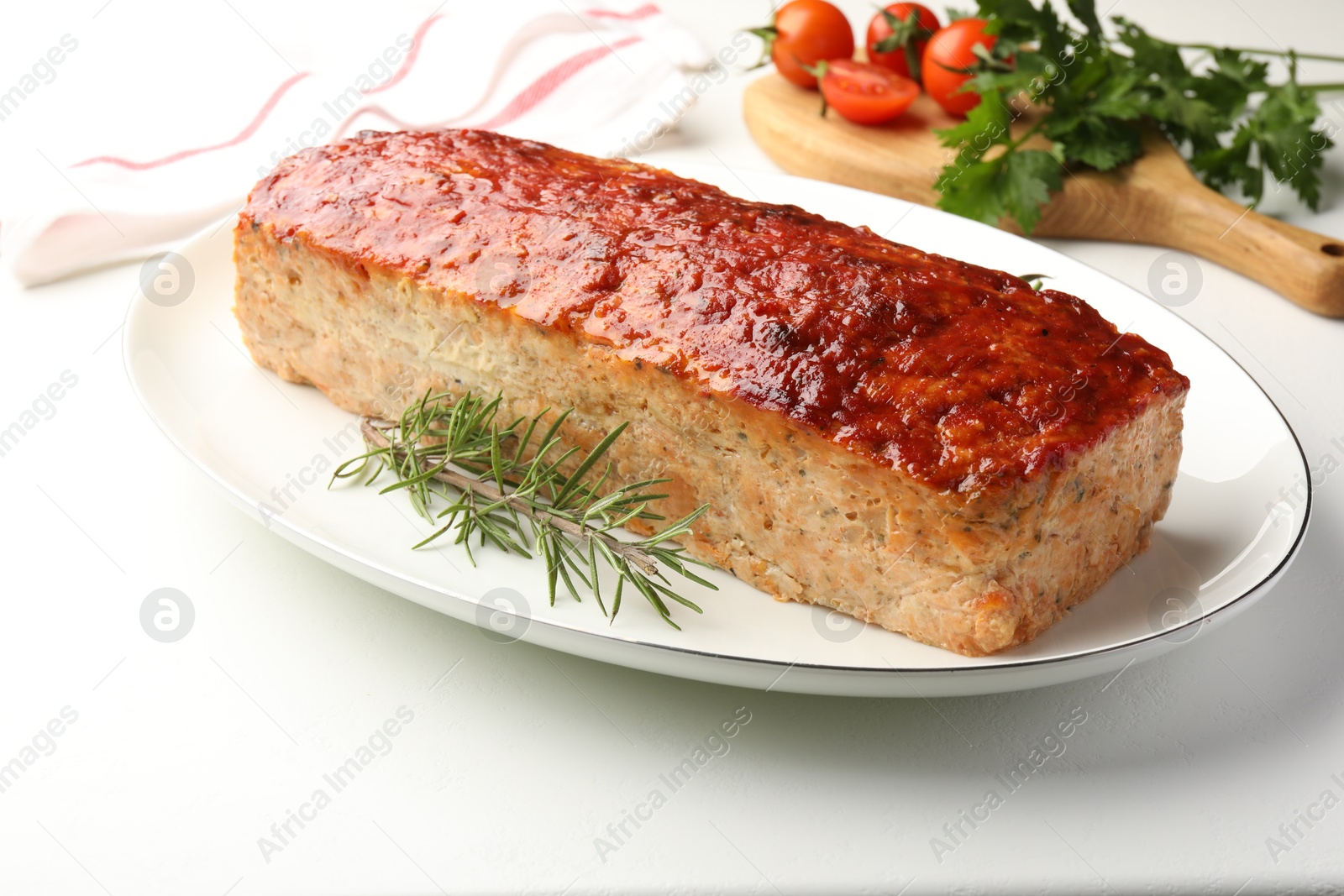 Photo of Delicious baked turkey meatloaf, rosemary, cherry tomatoes and parsley on white table, closeup