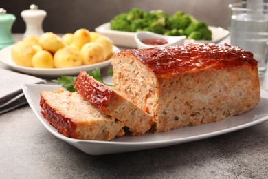 Photo of Delicious baked turkey meatloaf with vegetables served on grey table, closeup