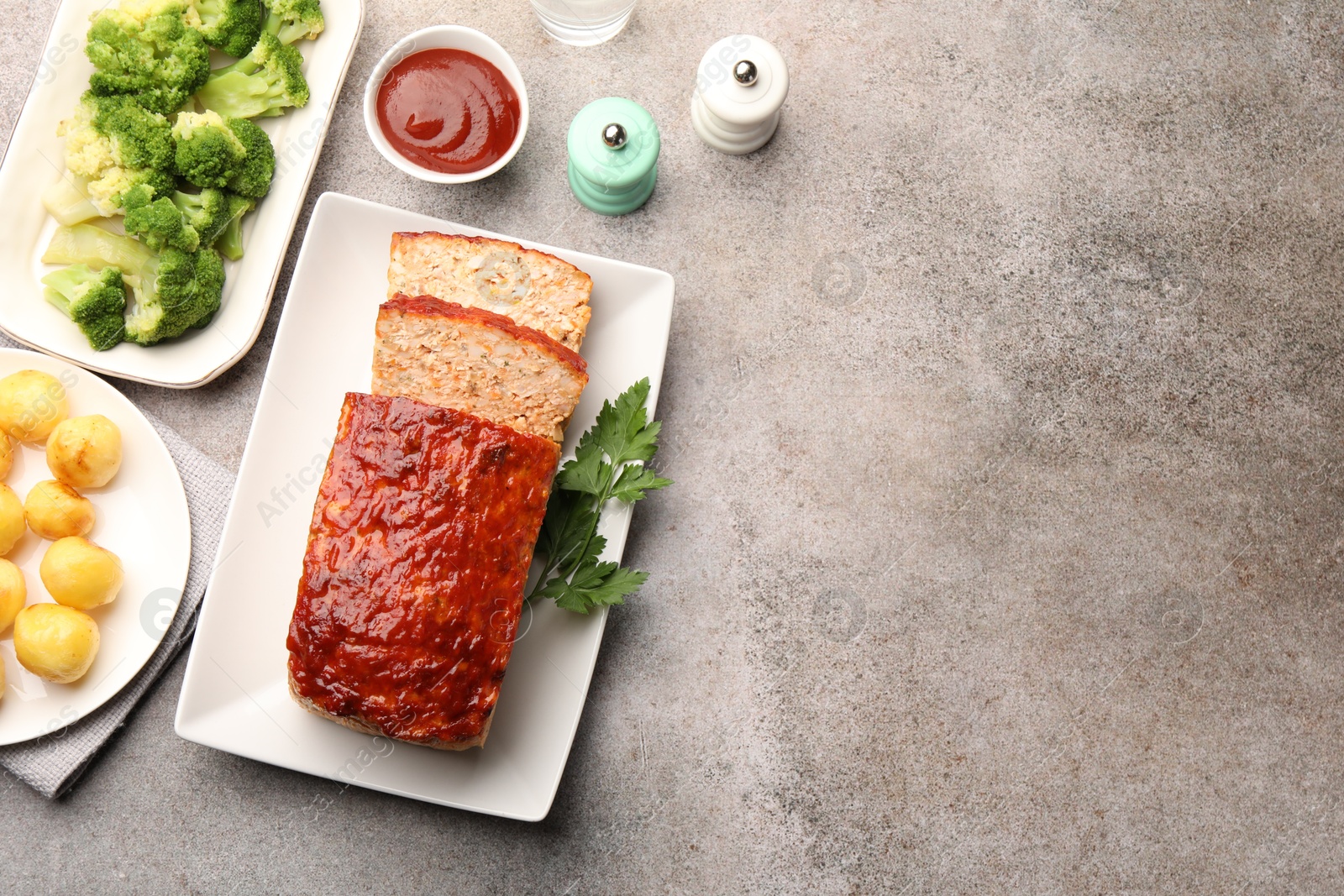 Photo of Delicious baked turkey meatloaf with vegetables served on grey table, flat lay. Space for text