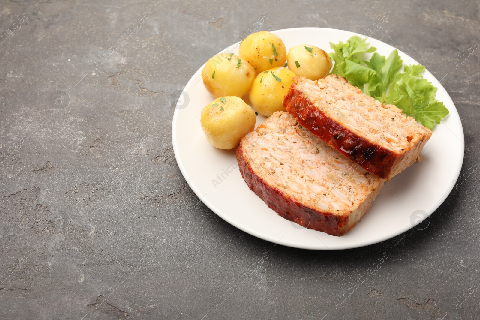 Photo of Delicious baked turkey meatloaf, potatoes and lettuce on grey table, space for text