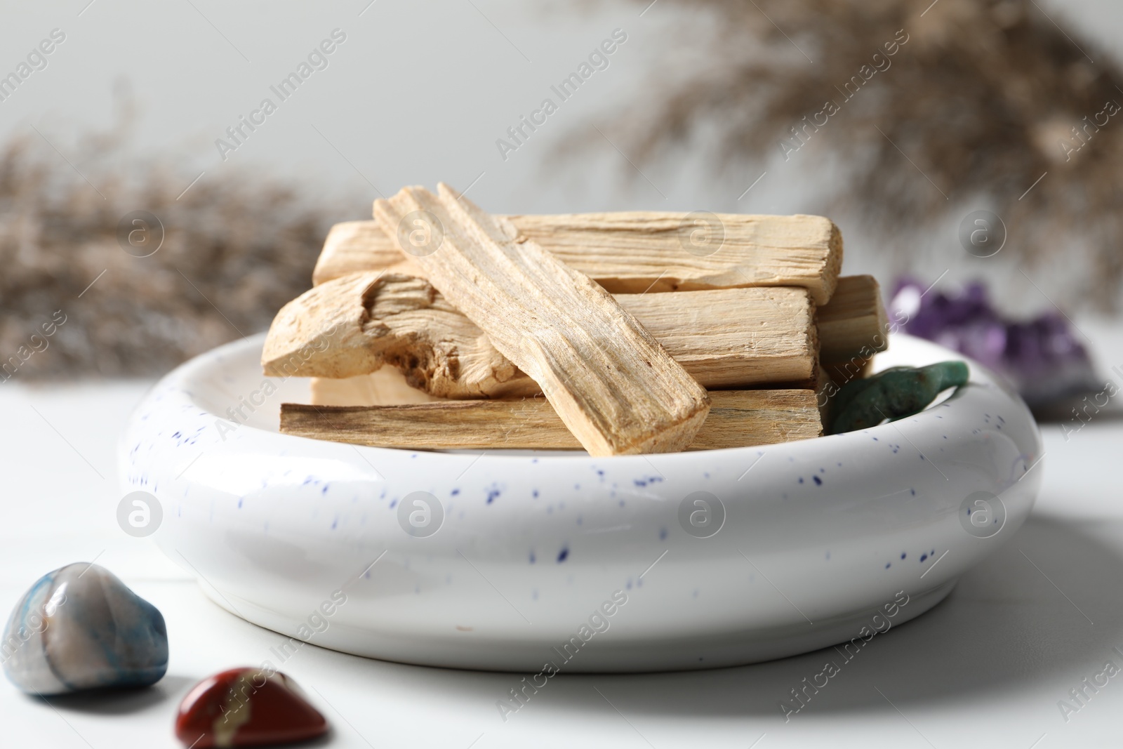 Photo of Palo santo sticks and gemstones on white table, closeup