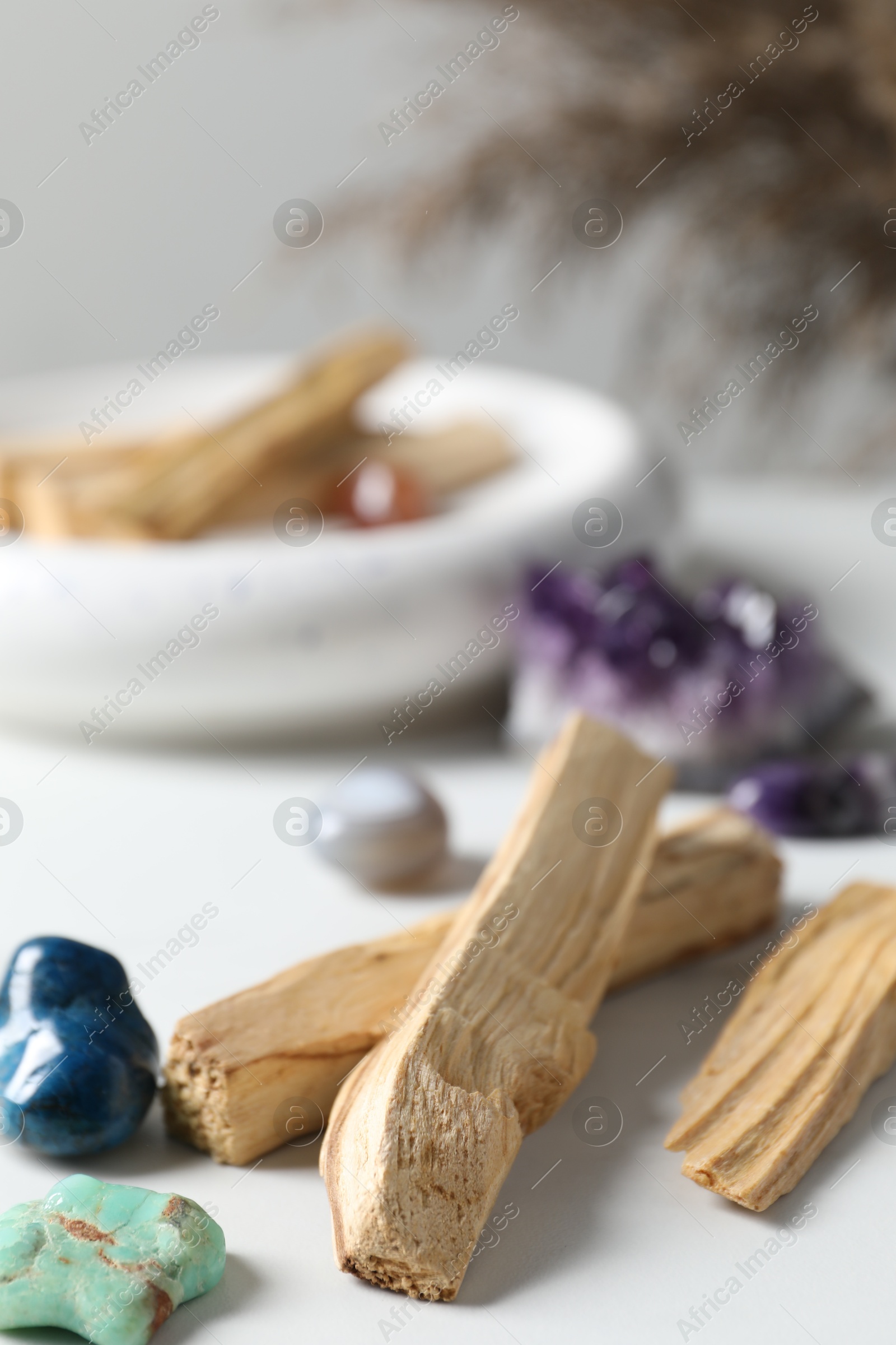 Photo of Palo santo sticks and gemstones on white table, closeup