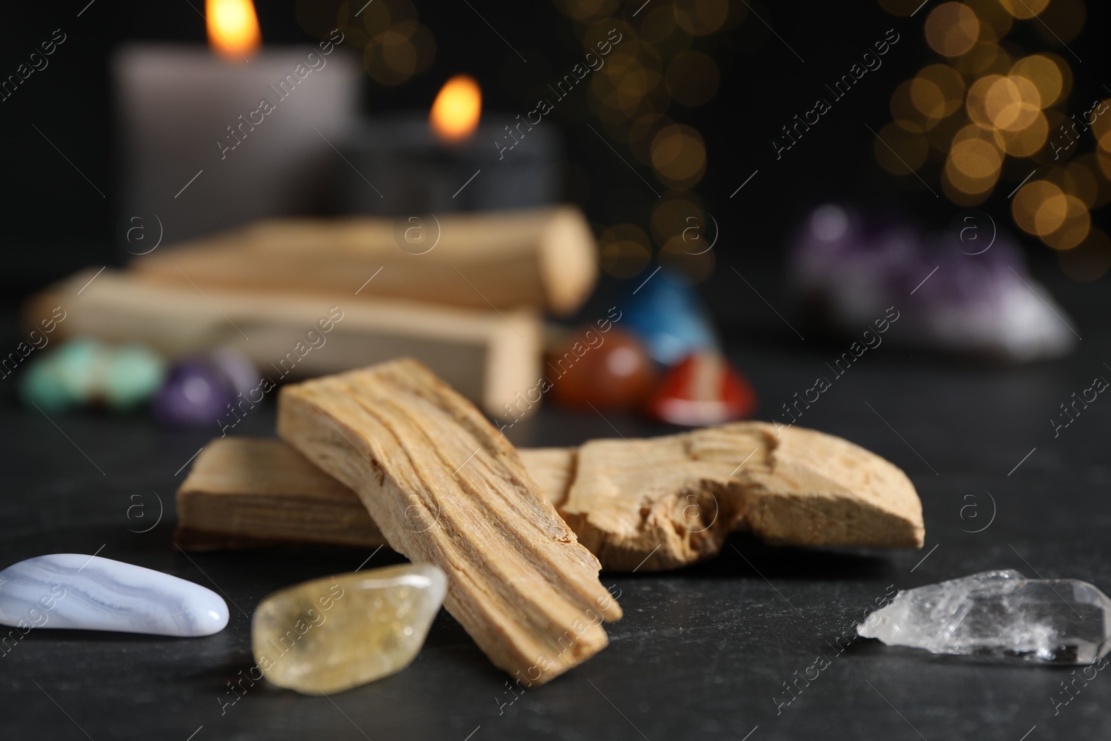 Photo of Palo santo sticks, gemstones and burning candles on black table against blurred lights, closeup