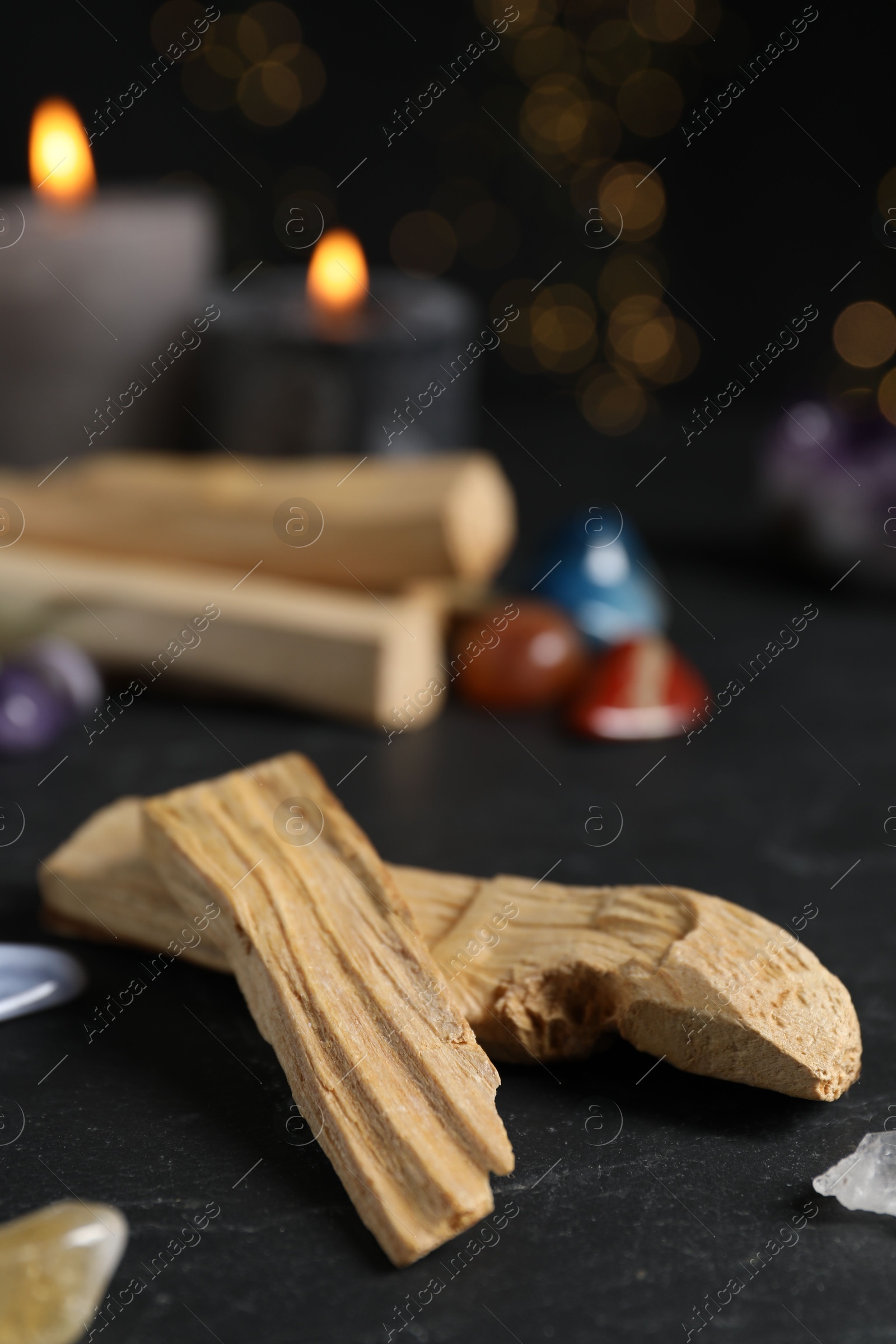 Photo of Palo santo sticks, gemstones and burning candles on black table against blurred lights, closeup